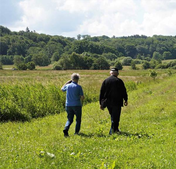 Zwei Erwachsene spazieren im Sonnenschein auf dem grünen Ådalweg bei Ravningeboen.